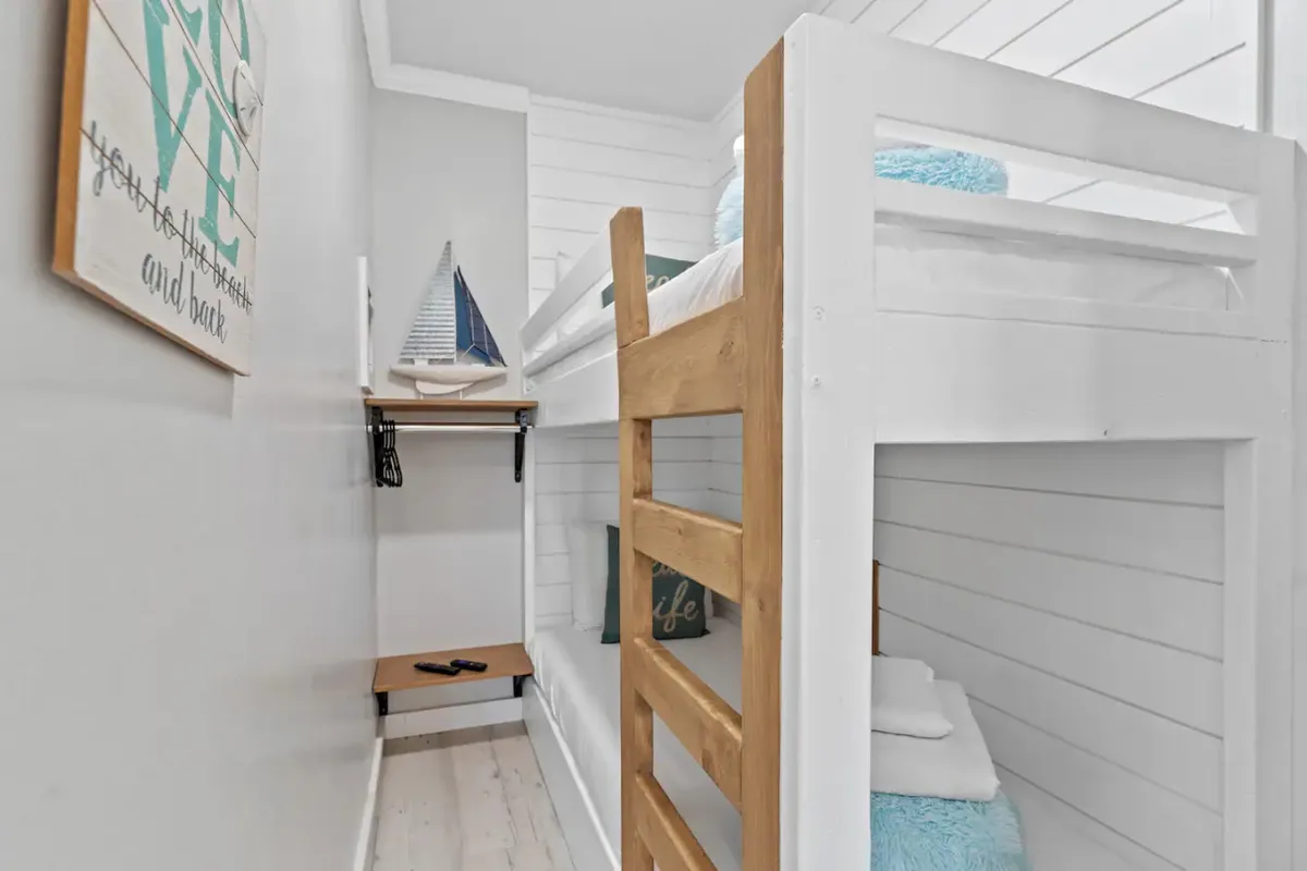 A playful bunk room featuring a sturdy bunk bed with nautical decor and a wooden shelf, well-suited for kids or friends. The setting feels cozy and inviting, designed for both restful sleep and quiet play or reading.
