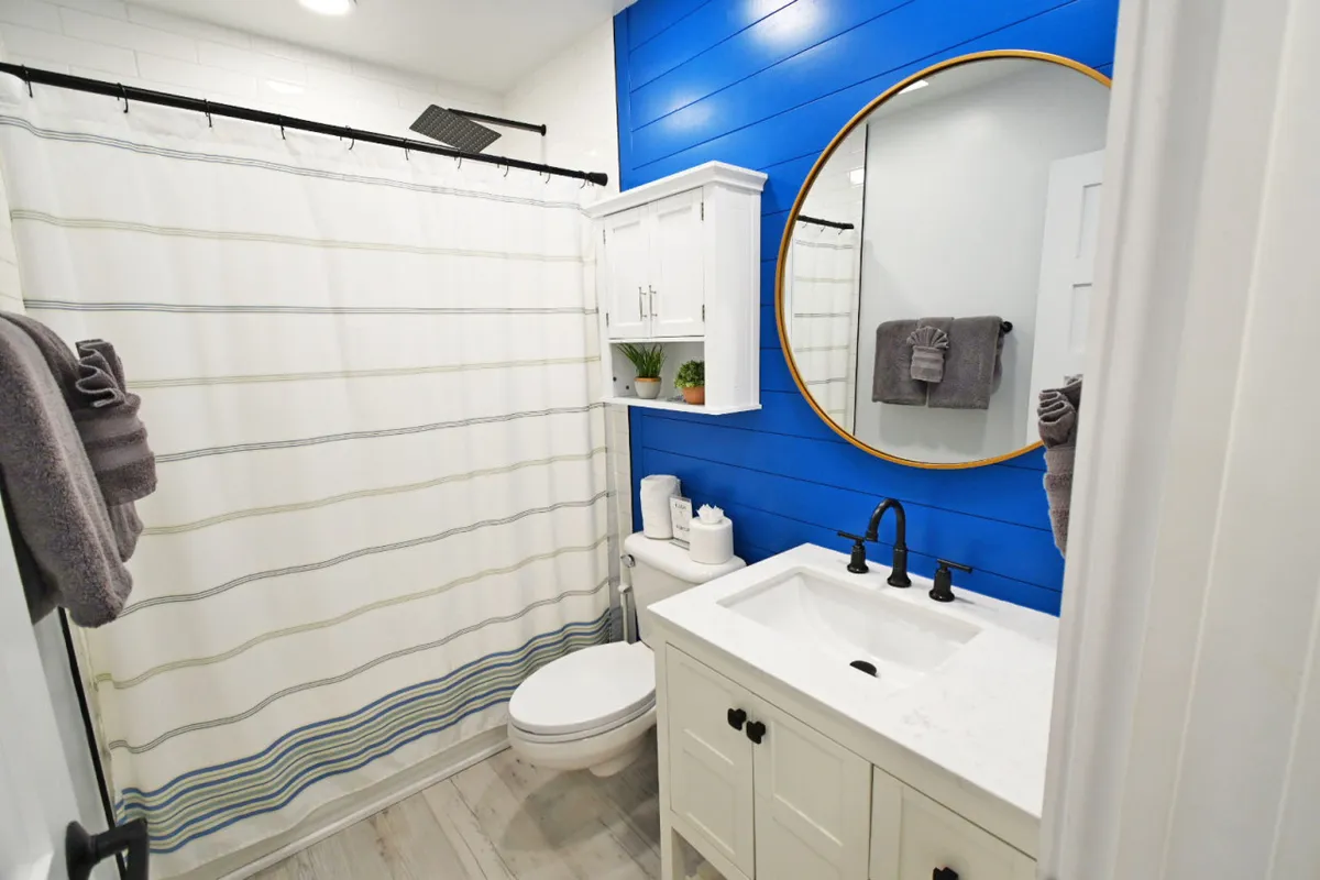 A modern bathroom featuring a blue accent wall, a round mirror, and a vanity with a sink. The ambiance is bright and inviting, suggesting a clean and refreshing environment ideal for self-care routines.