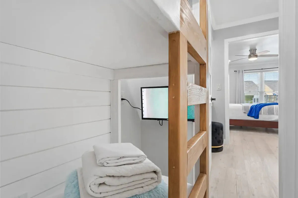 Open shelving with neatly folded towels and a small TV, with a view into a bedroom area. The functional storage hints at a well-organized closet or adjacent storage space stocked with essentials.