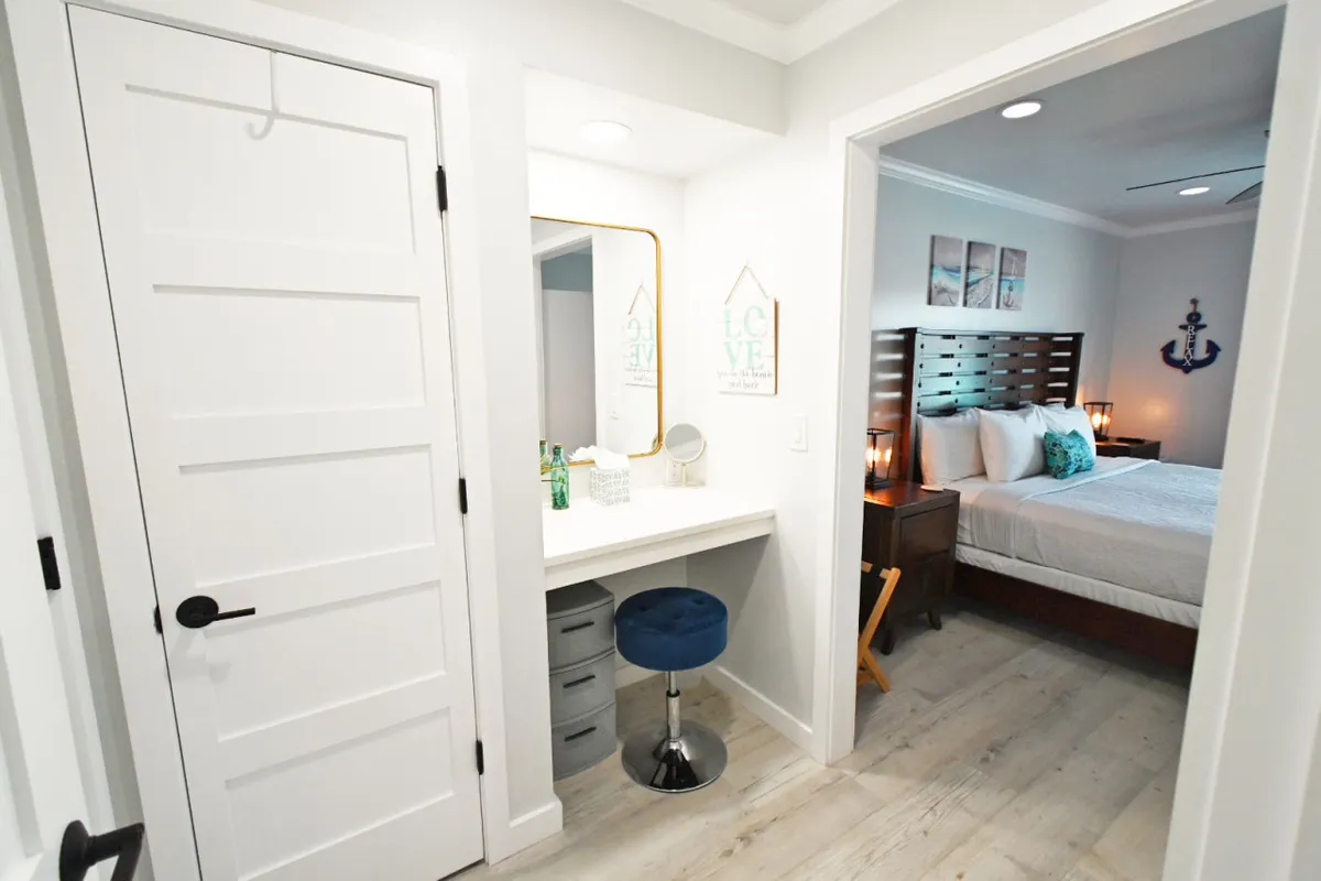 A calm and serene area with a vanity and mirror, decorative anchor and artwork, and a glimpse of the adjoining bedroom in the background. The space is designed for getting ready, working, or enjoying a moment of quiet reflection.