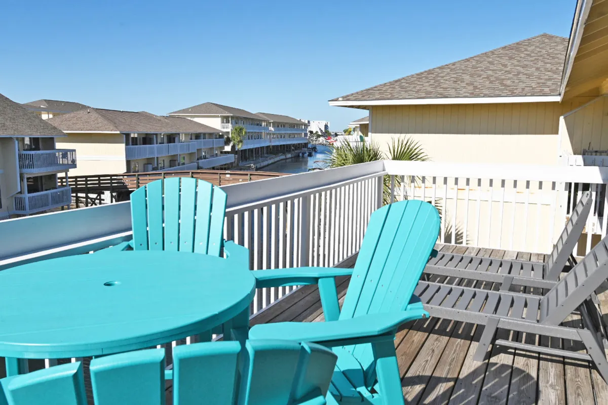 A serene waterside deck featuring a turquoise table and chairs, with views of the canal and surrounding residential buildings. The scene evokes a sense of peaceful outdoor living, ideal for watching boats drift by or enjoying meals with friends in a tranquil setting.