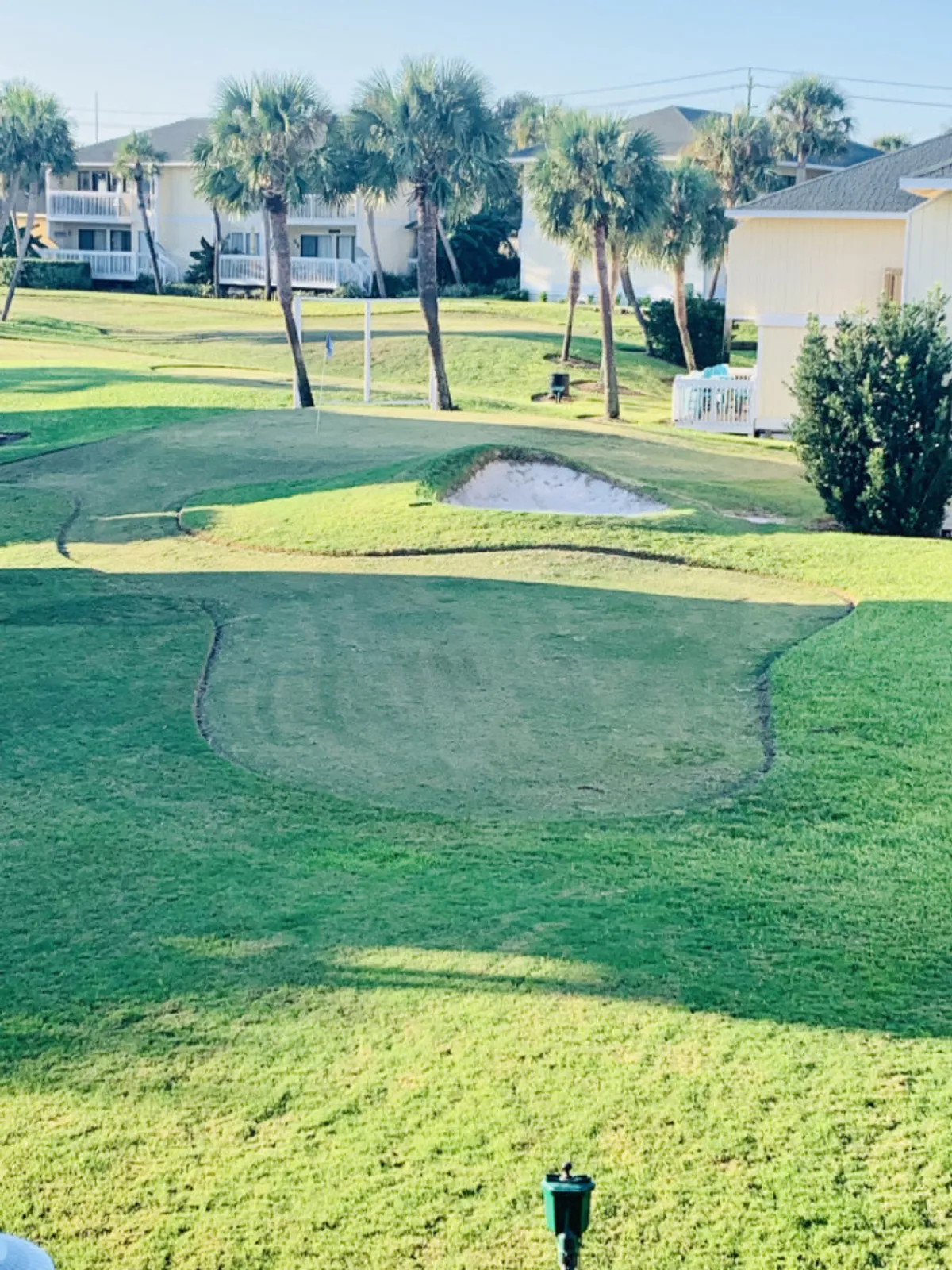 A well-maintained golf course green is framed by palm trees and bordered by attractive vacation homes. Benches and a soft sunrise glow add to the welcoming atmosphere, implying opportunities for gentle recreation and family togetherness.