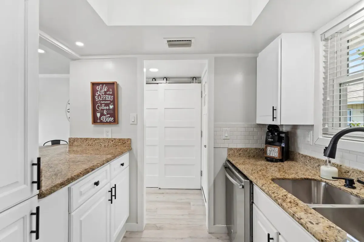 A close-up of the kitchen area highlights granite countertops, white cabinets, and a coffee maker, creating an intimate view of the culinary space. A decorative sign adds a cozy, personal touch, emphasizing the kitchen’s functionality and homey atmosphere.