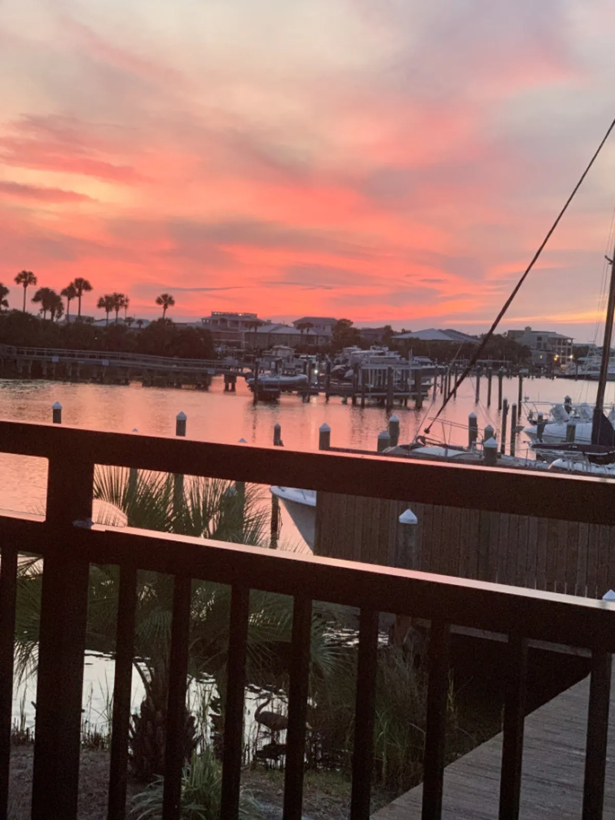 A breathtaking sunset scene over the tranquil canal, with shades of pink and orange reflecting on the calm water. Boats are docked at marina slips, and silhouetted palm trees and buildings are visible in the background, evoking a peaceful, romantic waterfront atmosphere.